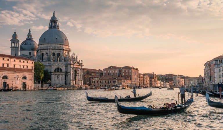 Gondolas on the waters of Venetian lagoon during a pale pink sunset.