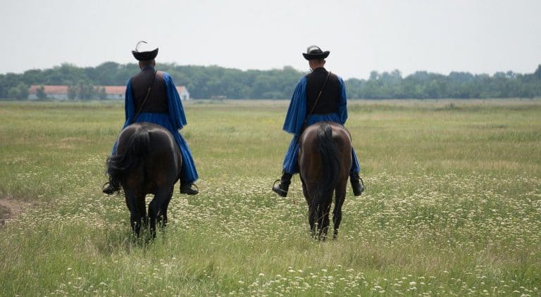 Two Hungarians on horseback riding away in Hortobagy National Park in Hungary, a day trip from Budapest.