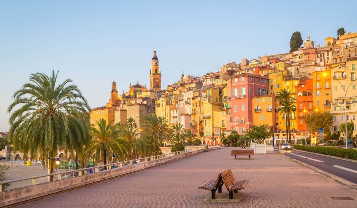 15 Best Things to do in Menton, France 1 Promenade along the water with colorful buildings and palm trees in Menton, France.