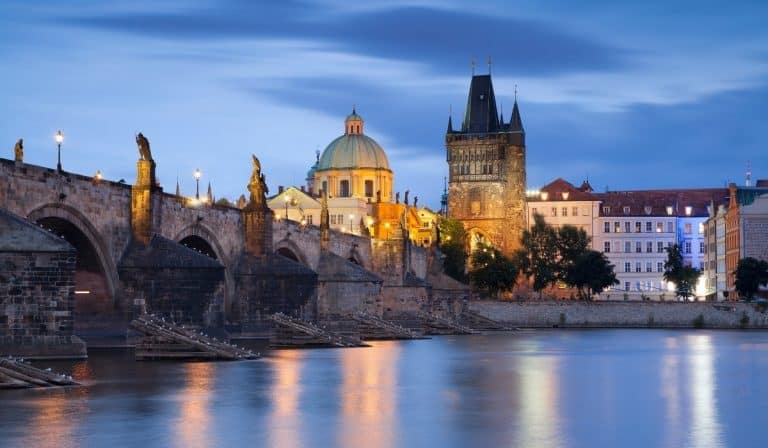 Prague bridge over river at dusk with the lights reflecting on the river.