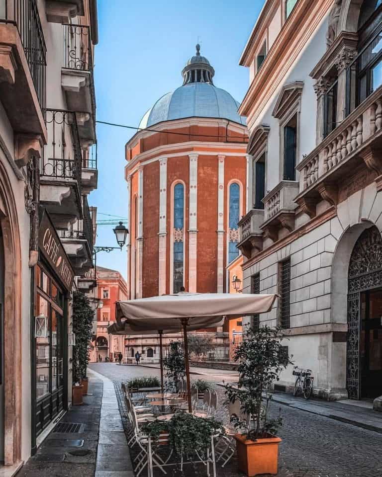 Blue domed Vicenza Cathedral seen at the end of a street with empty tables and chairs.